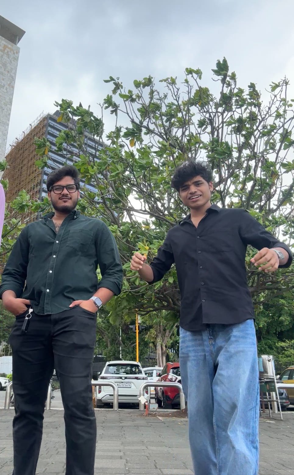 Two friends posing together outdoors near parked cars